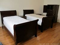 Pair of twin sleigh beds with white mattresses, showing dark mahogany wood and curved headboards and footboards.