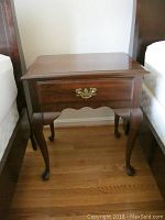 Front view of one nightstand showing single drawer and gold colored hardware, wooden construction with dark finish