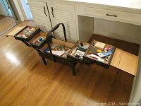 Photo showing open wooden sewing case with multiple tiers filled with sewing supplies