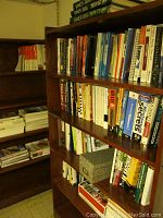 Wooden bookshelves filled with assorted computer and programming books, a small decorative storage box, and stacks of magazines on nearby shelves.