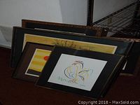 Five framed artworks stacked together, including a chicken lithograph visible on top