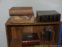 Full view of vintage books on wooden shelf, showing various sizes and wear including leather and hardcover editions.