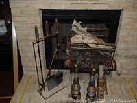 Full fireplace setup with tool holder containing poker, brush, shovel, metal log holder with fabric liner, and fireplace rug on floor.