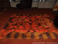 Full view of rectangular shag rug laid flat on floor, showing overall abstract orange/red/brown pattern and pile depth.
