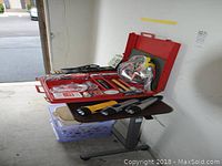 Photo showing red automotive safety kit case open with jumper cables, flashlight, voltage converter kit, first aid items, and other automotive tools on a rolling cart.