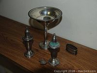 Photo showing sterling silver pedestal candy dish, two salt and pepper shakers, and pair of napkin rings on a wooden surface