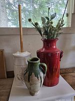 Three main vessels: butter churn with lid and dasher, red vase with stems, green jug vase