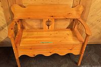 Front view of solid pine storage bench showing heart cutout, armrests, scalloped apron, honey finish