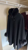 Front view of black cape coat with fur collar and cuffs