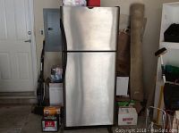 Frigidaire stainless steel top-freezer refrigerator front closed view in garage setting.