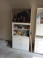 Full view of white storage cupboard with smoked glass upper doors and solid lower doors, containing coffee mugs, coffee grinder, ceramic Christmas tree lamp and other small decorative items on shelves.