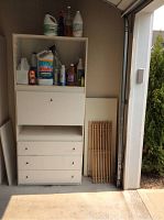 Full view of the white Ikea-style storage cabinet with secretary desk and drawers, showing cleaning supplies on shelves and marks on cabinet surfaces.
