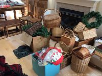 Photo showing a large group of assorted wicker baskets of various styles, shapes, and sizes on the floor near a fireplace with a Christmas wreath visible.