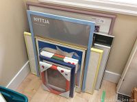 Multiple picture frames stacked together including unopened IKEA NYTTJA frames and other framed prints