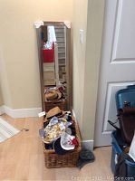 Framed vertical mirror leaning against wall with basket and scarves, hats scattered around