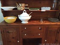 Overview of the shelves displaying all the serving ware items including the soup tureen, fish platter and plates, fish-shaped baking dish, pitcher, yellow bowl, ceramic bottles, cake stand, and trays.
