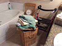 Wicker hamper with towels on top, red Evolution walker, clock, and bathtub corner visible