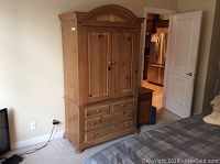 Full frontal view of the Broyhill wooden armoire entertainment unit positioned in a bedroom showing the front doors, drawers, and carved crown molding.