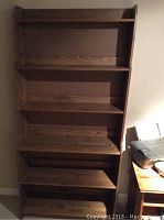 Front view of the tall wooden bookcase with five shelves, showing scratches and wear.