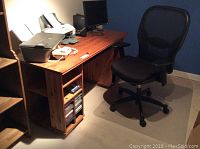 Photo of the entire wooden computer desk with several items on top not included in the sale, next to black mesh swivel office chair.