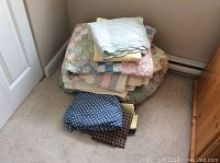 Overview of stacked bed linens including patchwork quilt, white quilt, duvet covers, pillow shams, and fabric pieces