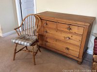 Overall view of the wooden dresser and wooden chair side by side on carpeted floor against a wall.