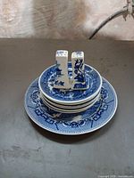 Stack of six willow pattern plates with salt and pepper shakers on top