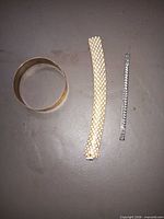 All three bracelets laid out: brass bangle, gold mesh bracelet, silver chain bracelet