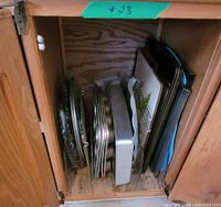 Cabinet interior showing stacked glass platters, muffin pans, cake pans, and trays