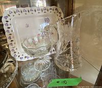 Platter, pedestal dish, and crystal pitcher grouped together inside display cabinet