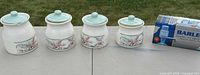 Four floral ceramic canisters with green lids lined up