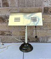Front view of brass banker’s lamp showing vented shade, pull chain, base and cord