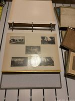 Open photo album showing adhesive page with mounted black-and-white photos and stack of metal frames beside