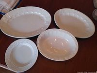 Four of the white ceramic pieces showing embossed grape motif: two platters, one bowl, one plate