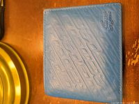 Closed wallet front showing textured blue leather and embossed Lacoste logo