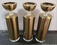 Front view of three matching brass-finish cylindrical candle holders with acrylic accents