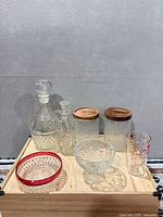 Group shot of all glass items including decanter, cruet, two jars with lids, red-rim bowl, compote, measuring beaker