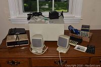 Wide view of office electronics on wooden table including speakers, calculators, clock radios, and lanyards