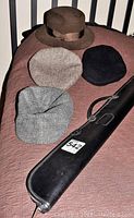 All hats and pool cue case on a pinkish-brown quilted blanket, lender added lot number sticker 542.