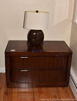 Wooden two drawer nightstand with oval ceramic base lamp on top