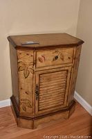 Front view of decorated wooden cabinet with drawer and door, showing floral paint design and hardware.