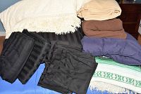 Image showing assorted bed linens including black sheets and comforter, beige and brown blankets, and a blue pillowcase set.