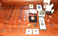 Overview of all religious jewelry items including necklaces, pins, pendants, and bracelet laid out on wooden surface