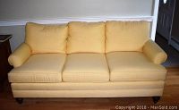Front view of three-seat yellow Sunbrella fabric sofa with three seat cushions and three back cushions, and rolled armrests.