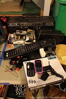 Overview of vintage Sony cassette deck stacked with cassette tapes, various electronics including a long black remote and small black walkie talkie.