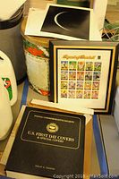 View of framed 2000 Legends of Baseball stamp sheet, black binder labeled U.S. First Day Covers, and popcorn tin with stamps.