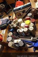 Photo showing various cans of adhesives, caulking tubes, and spray paint cans grouped on a table