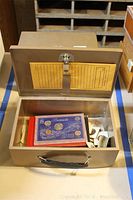 Open metal cash box containing a Bermuda coin collection display, assorted coins and currency, thread and shears