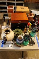 Wide view of the lot showing wooden cigar boxes stacked, ceramic vases, green glass candle holders, aerosol spray can and other items on a table