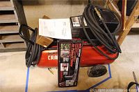Red Craftsman air compressor with black motor housing and wheels shown with boxed air pressure washer kit and paper manual on top.